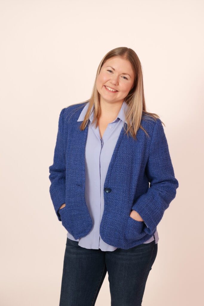 Iitu Leinonen Piasentier seisoo kädet jakun taskussa, katsoo kameraan ja hymyilee.